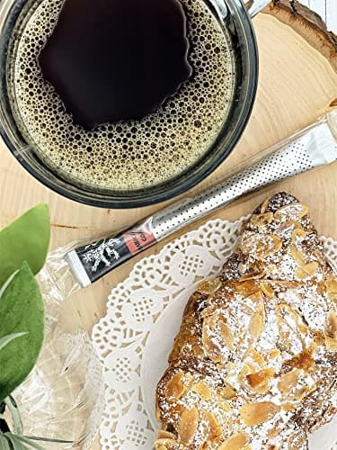 Arabica Gold Coffee — on wood slice beside glass mug of foamy brewed coffee, almond croissant, doily, foliage