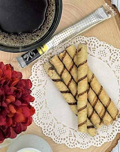 Hazelnut Arabica Coffee — on wood board beside dark glass mug of coffee, chocolate-swirl wafer rolls, red flower, doily